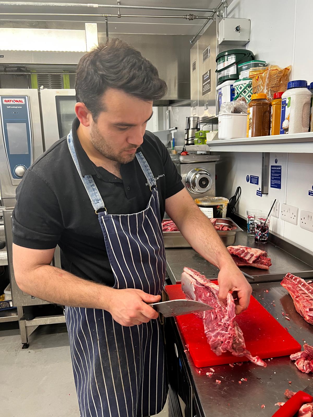 Mikail breaking down a rack of lamb ribs on a red board