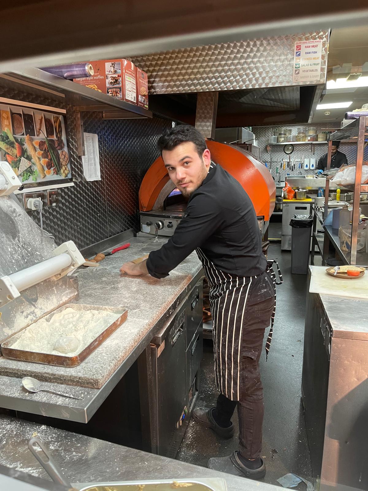 Mikail rolling dough beside a domed oven