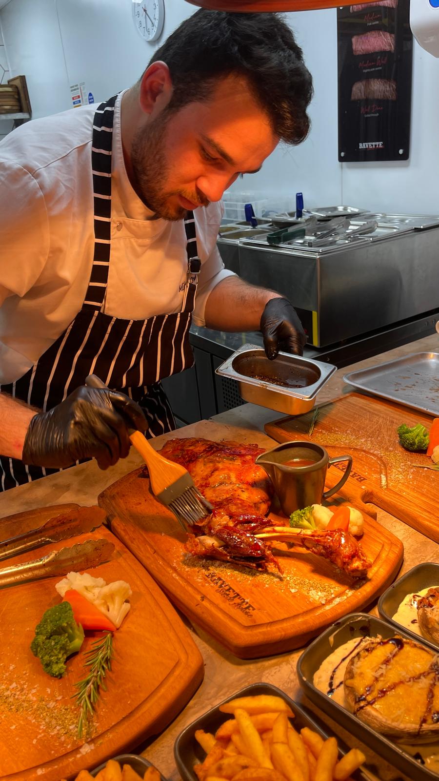 Mikail glazing a lamb shoulder on a sharing board with sides