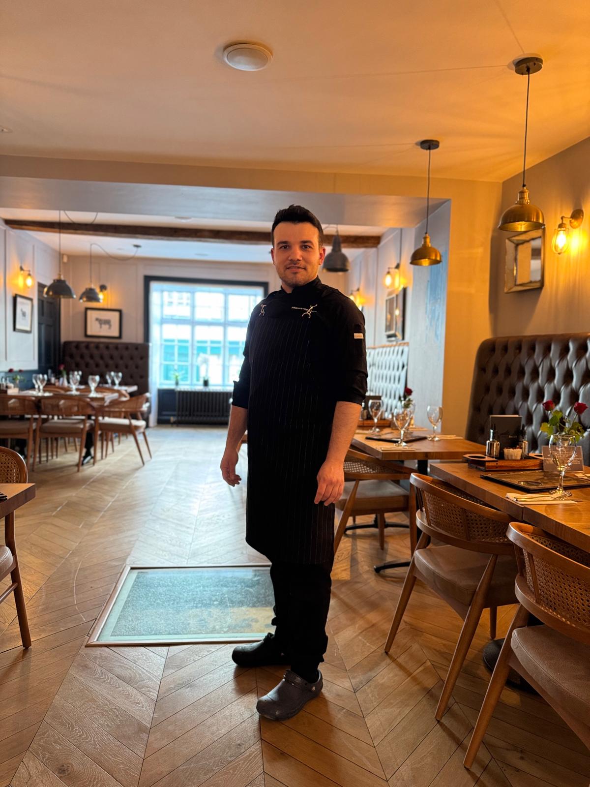 Mikail Ceyhan in chef's blacks, standing in a restaurant dining room