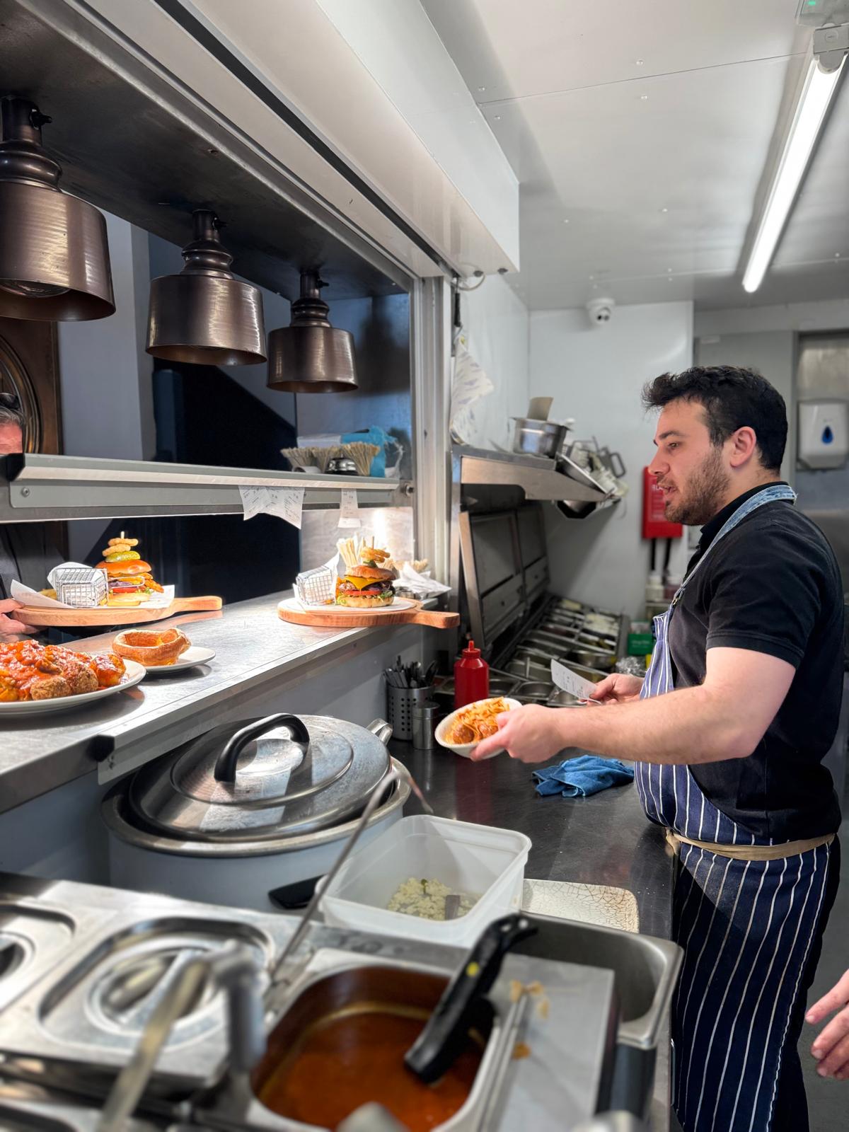 Stacked burgers and pasta waiting under the heat lamps on the pass